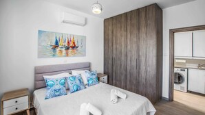 Ein modernes Schlafzimmer mit Bett, einem Segelboot-Gemälde, einem Kleiderschrank und einem sichtbaren Waschbereich.