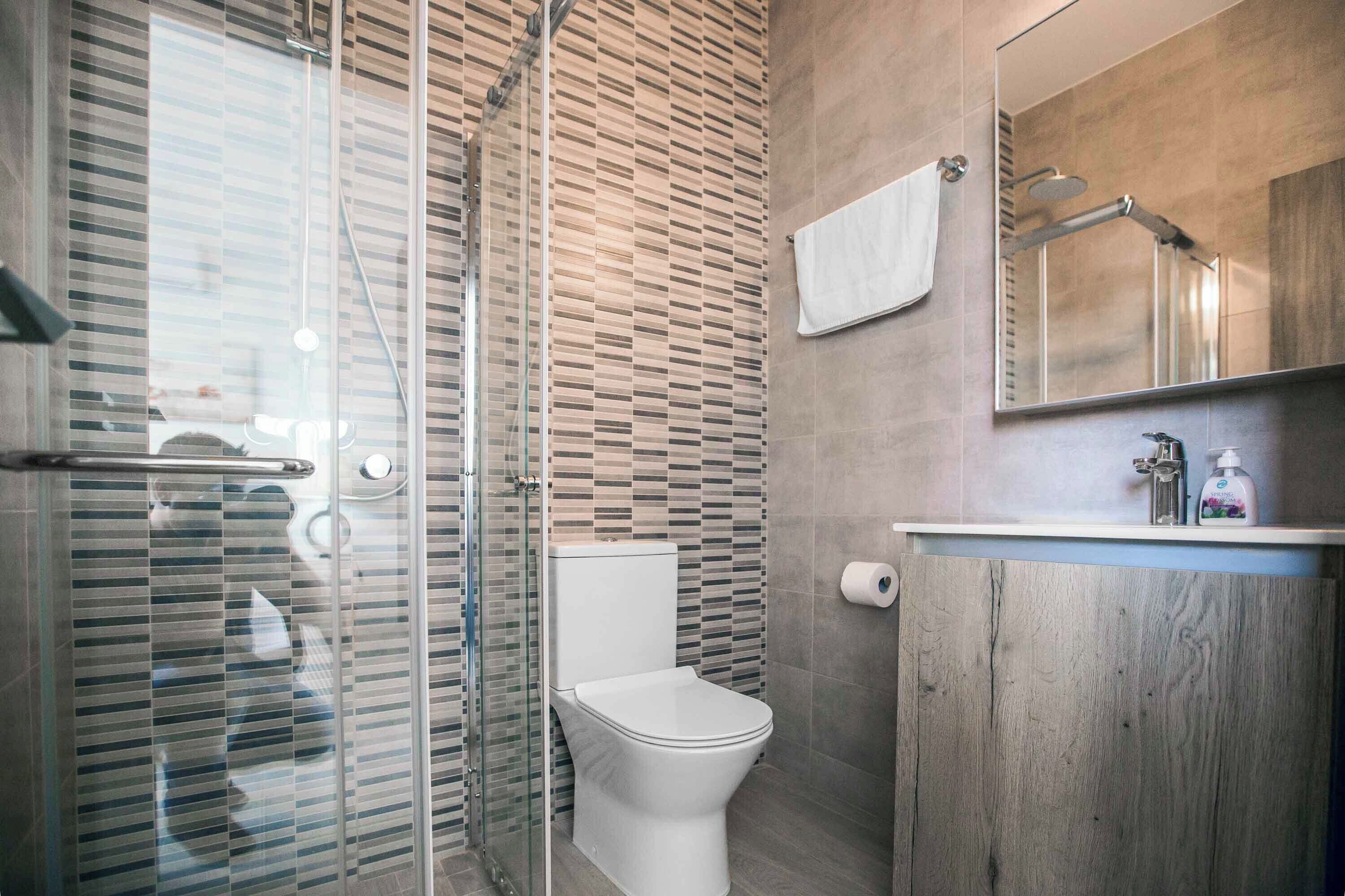 Une salle de bain moderne avec une douche à parois de verre, des toilettes blanches et un meuble-lavabo en bois avec un miroir.