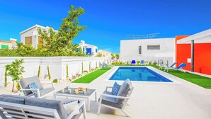 Ein moderner Poolbereich im Freien mit weißer und blauer Möbel, blauem Himmel und gepflegtem Rasen.
