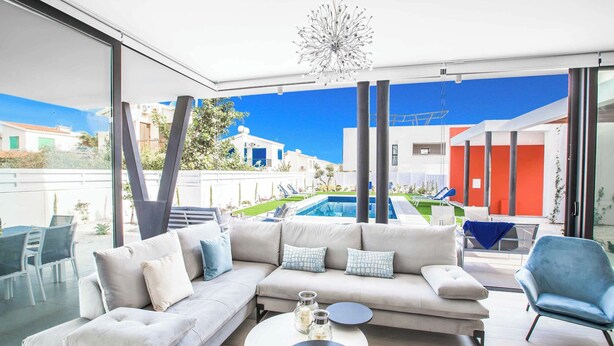 Ein modernes Wohnzimmer mit einer großen Couch, einem Couchtisch und Blick auf einen Pool sowie Gebäude.