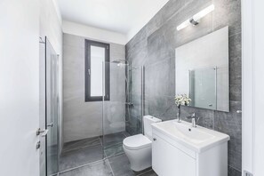 Un baño moderno con cabina de ducha de vidrio, inodoro y lavamanos con espejo.
