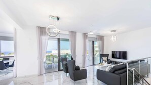 A modern living room with a sofa, chairs, a TV, and a balcony with curtains.