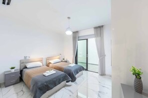 Un dormitorio moderno con dos camas, una mesita de noche, una planta en maceta y un ventanal corredizo al balcón.