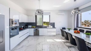 A modern kitchen with a dining area, featuring a large window, stainless steel appliances, and a marble floor.
