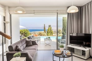 Ein modernes Wohnzimmer mit einer Couch, einem Fernseher und Blick auf einen Pool.