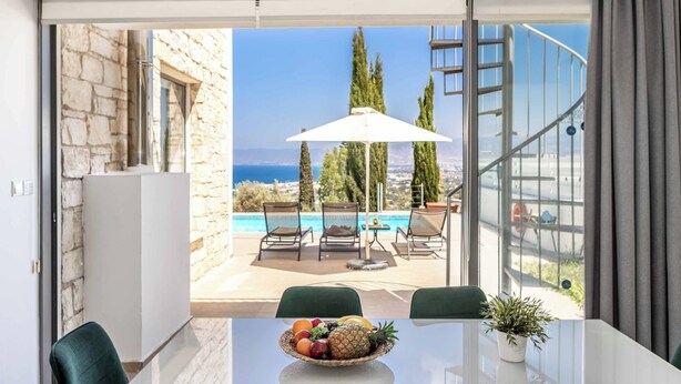 A modern room with a glass door leading to a balcony with a pool, outdoor furniture, and a view of the sea. - Villa Latchi View - Three Bedroom Villa, Sleeps 6 (Neo Chorio)
