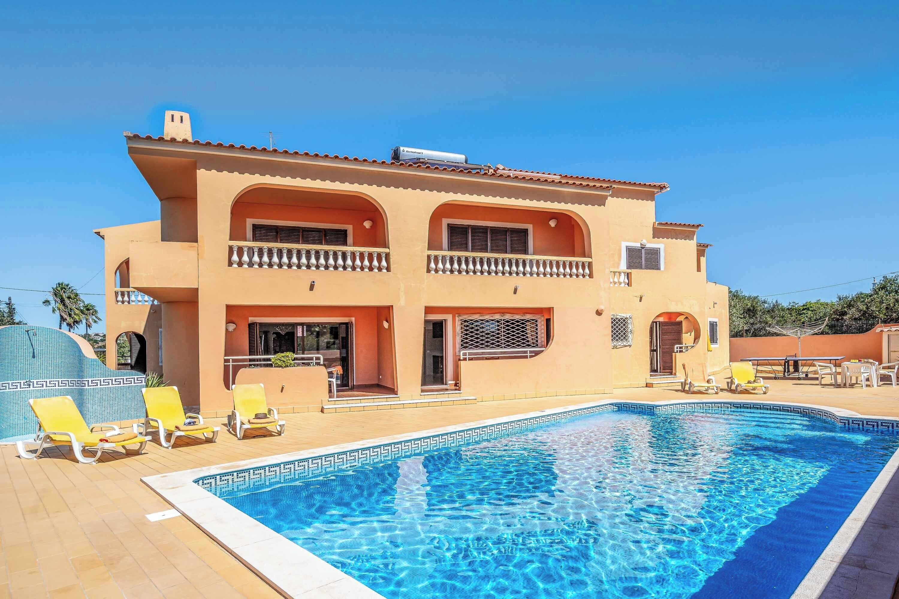 A two-story building with a swimming pool, outdoor seating, and a clear blue sky.