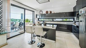 A modern kitchen with a central island, black cabinets, and a large window overlooking a balcony. - Villa Sunset Vista - Three Bedroom Villa, Sleeps 6 (Pêra)