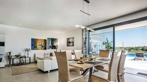 A modern living room with a dining area, featuring wicker furniture, a white sofa, and artwork on the walls. - Villa Sunset Vista - Three Bedroom Villa, Sleeps 6 (Pêra)