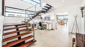A modern interior with a wooden staircase, a desk area, and a view through large windows. - Villa Sunset Vista - Three Bedroom Villa, Sleeps 6 (Pêra)