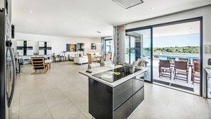 A modern kitchen with a central island, a dining area with a view, and a living space with a large window. - Villa Sunset Vista - Three Bedroom Villa, Sleeps 6 (Pêra)