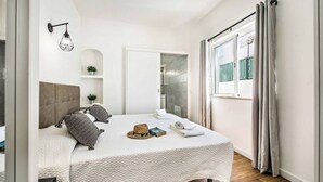 Ein modernes Schlafzimmer mit einem großen Bett, einem Nachttisch, einer Wandleuchte und einem Fenster mit Vorhängen.