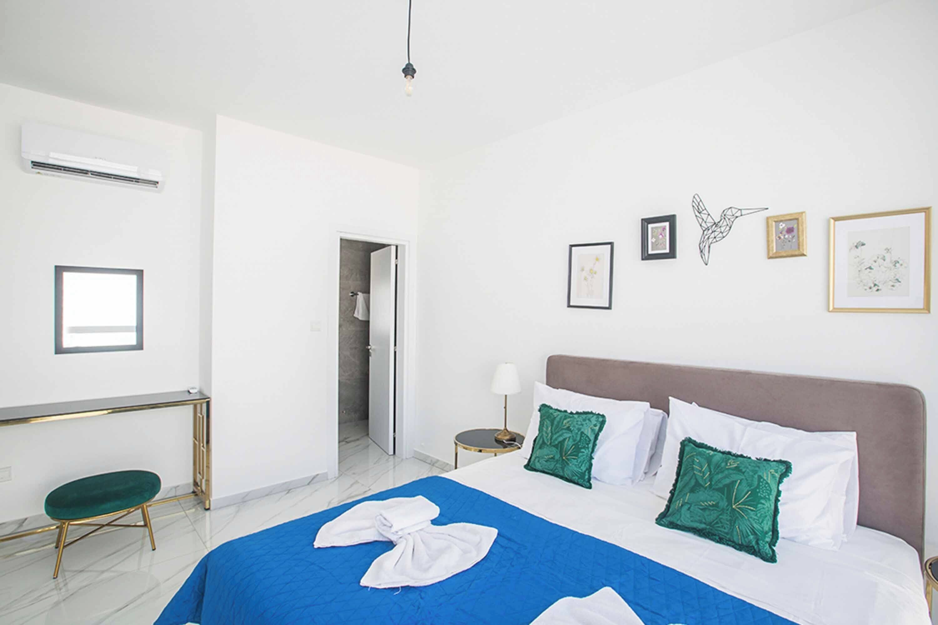 Una camera d'albergo con un letto, una scrivania, una sedia, un comodino e una porta che dà su un bagno.