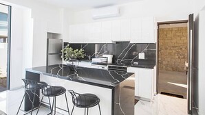 A modern kitchen with a marble island, black bar stools, and a brick wall visible through an open door. - Vie Bleu 1 - Four Bedroom Villa, Sleeps 8 (Πρωταράς)