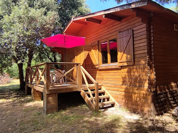 A wooden cabin with a deck, stairs, and a red umbrella.