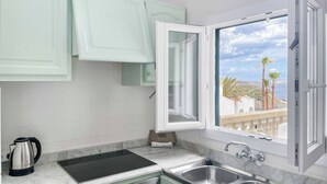 A kitchen with a window, a kettle, and a sink.