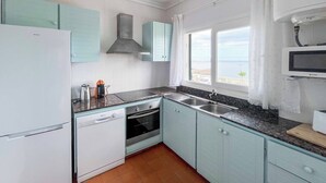 Una cocina con electrodomésticos blancos, armarios verde mar, una estufa y un ventanal con vistas.