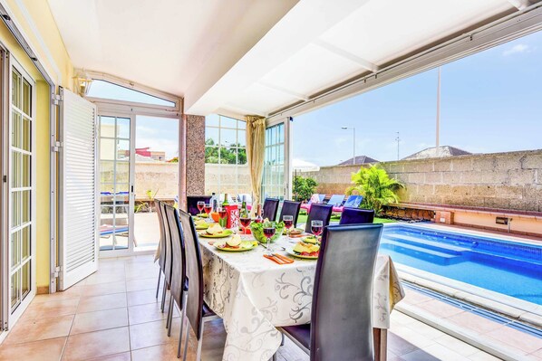 Enjoy a casual meal with a poolside view from this outdoor dining area, sheltered by a retractable roof.