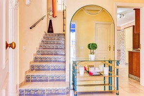 Staircase leads to an upper level, flanked by a glass table and a potted plant.