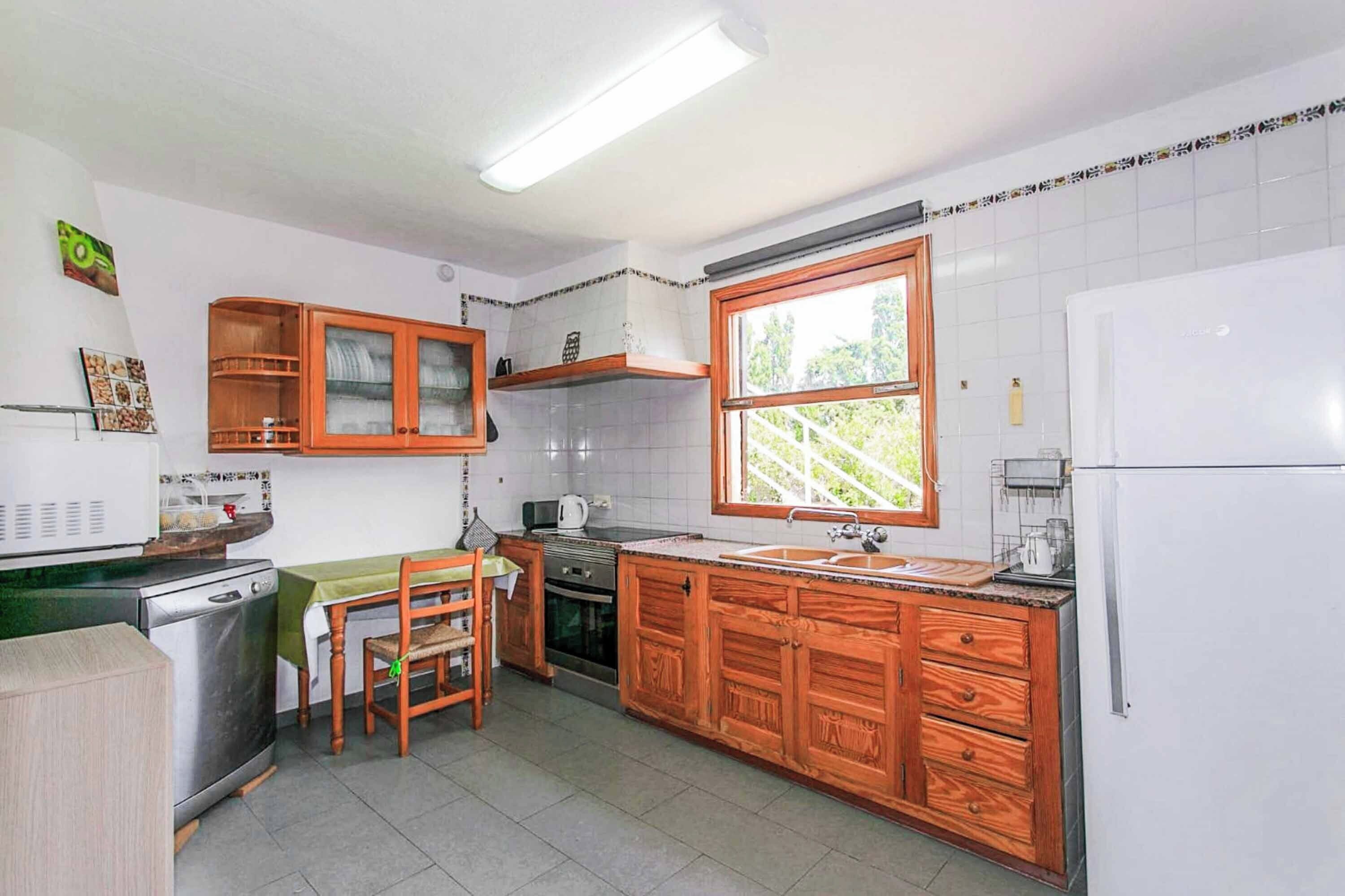 A compact kitchen with wooden cabinets, a built-in oven, a refrigerator, and a window providing natural light.