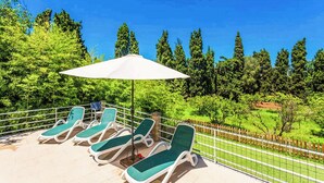 Ein Poolbereich mit Liegestühlen und einem Sonnenschirm, umgeben von einem Zaun und viel Grün.