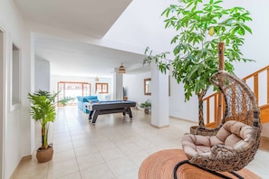 A spacious living area with a pool table, a hanging chair, and a large potted plant.