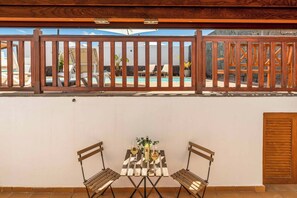 A patio with a wooden fence, a table with two chairs, and a view of a pool and lounge chairs. - Villa Samui - Four Bedroom Villa, Sleeps 8 (Playa Blanca)