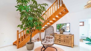 A spacious living area with a wooden staircase, a hanging chair, a large potted plant, and a wooden cabinet. - Villa Samui - Four Bedroom Villa, Sleeps 8 (Playa Blanca)