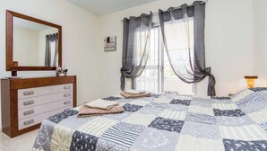 A bedroom with a bed, a dresser, a mirror, and a window with curtains.