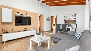 Una sala moderna con un sofá gris, mueble blanco para entretenimiento y un televisor montado en la pared.