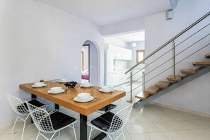 Un coin repas avec une table en bois, des chaises blanches et un escalier.