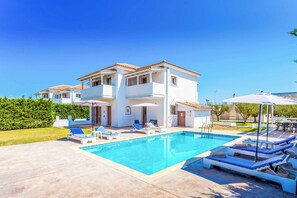 Une maison à deux étages avec une piscine, un espace salon extérieur et un ciel d’un bleu éclatant.