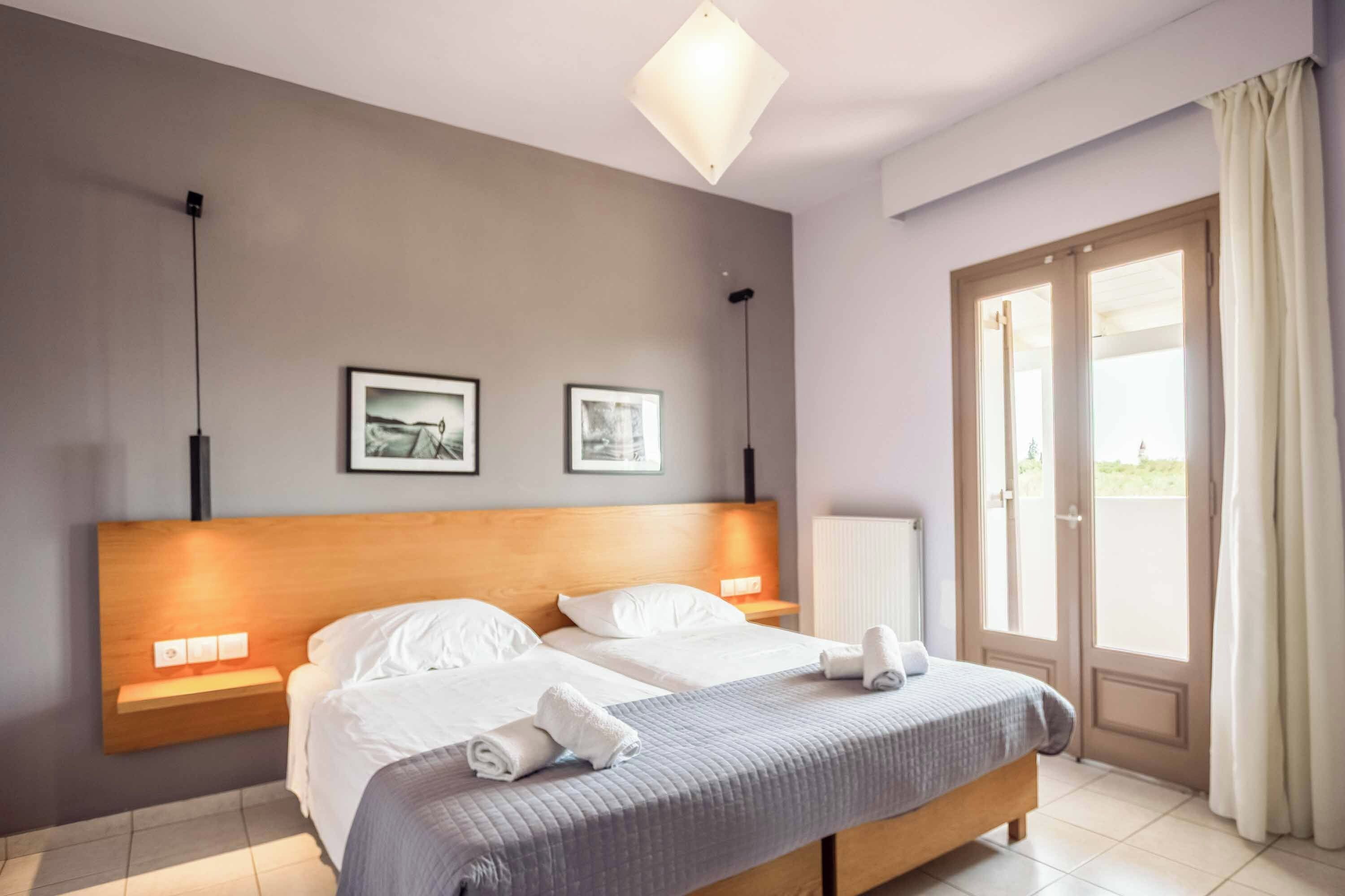 Een hotelkamer met een tweepersoonsbed, twee nachtkastjes, een radiator, een raam met gordijnen en twee ingelijste foto's aan de muur.