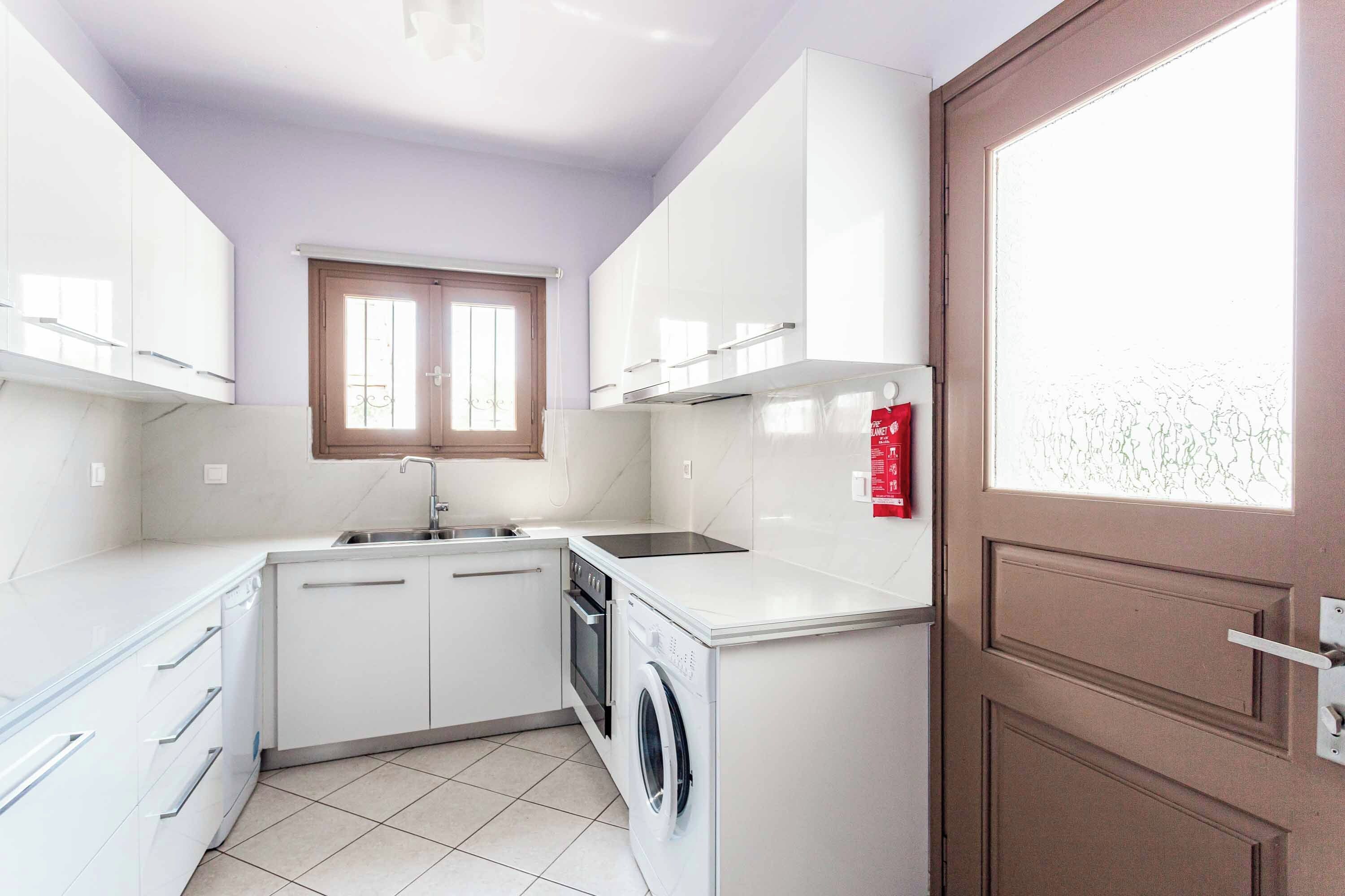 Une cuisine compacte avec des meubles blancs, un lave-vaisselle intégré et un lave-linge.