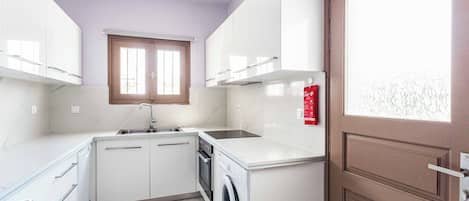 Une cuisine compacte avec des meubles blancs, un lave-vaisselle intégré et un lave-linge.