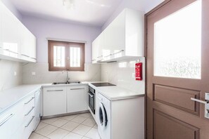 Une cuisine compacte avec des meubles blancs, un lave-vaisselle intégré et un lave-linge.