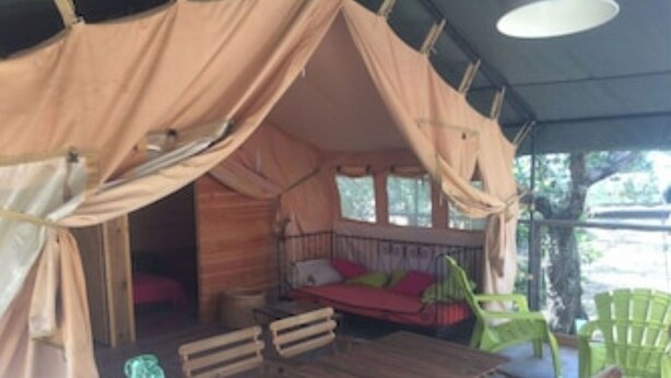 Una carpa con una mesa y sillas de madera, un banco y una botella.