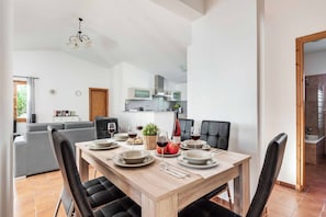 A dining area with a wooden table set for four, surrounded by black chairs. A kitchen is visible in the background with modern appliances. - Villa Paco - Three Bedroom Villa, Sleeps 6 (Ciutadella de Menorca)