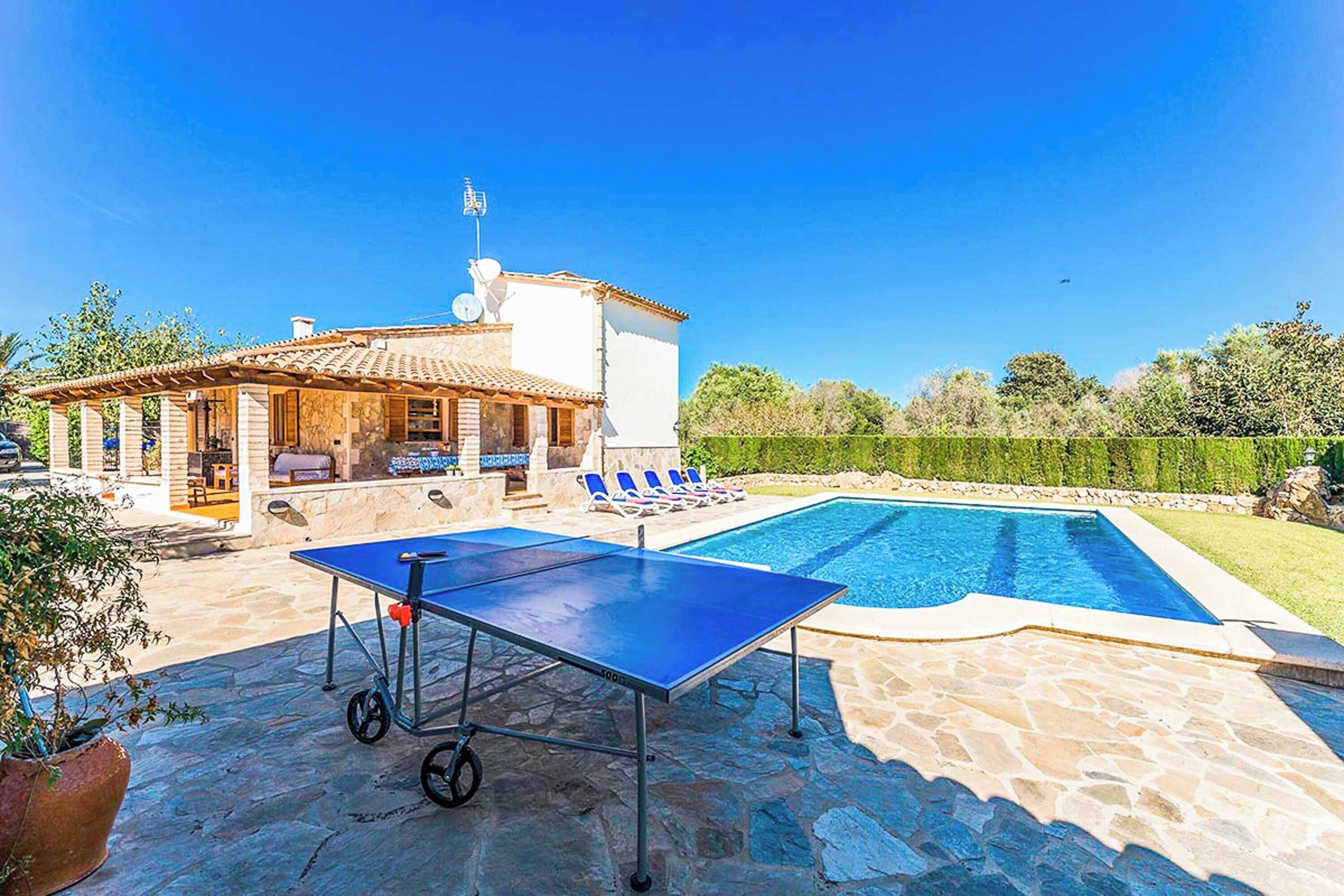 A pool area with a ping pong table, lounge chairs, and a building with a tiled roof.