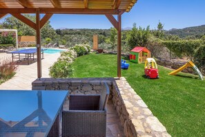 A covered outdoor area with a pool, a children's play area, and a view of the surrounding landscape.