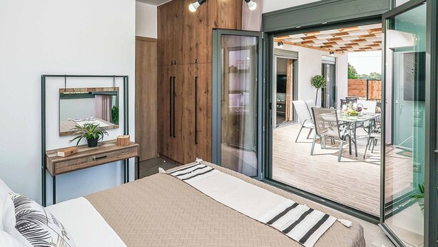 Ein modernes Schlafzimmer mit einem Bett, einem Holzschrank, einer Glastür zu einem Essbereich und einem kleinen Nachttisch mit Pflanze.