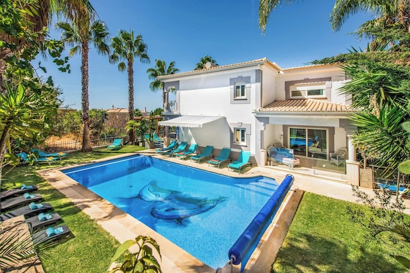 Relax by the pool in a tranquil oasis surrounded by lush greenery and palm trees.