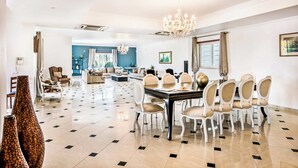 Een ruime eetruimte met een grote tafel, meerdere stoelen en een kroonluchter.