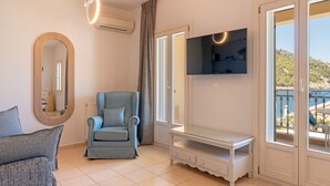 Una habitació amb una butaca gris, un petit taula blanca, un televisor fixat a la paret i un mirall gran.