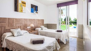 A hotel room with two beds, a wooden headboard, a window with a view of the outdoors, and artwork on the wall. - Villa Rachel - Three Bedroom Villa, Sleeps 6 (Es Mercadal)