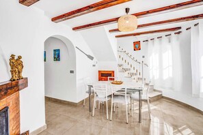 Comedor con una mesa y sillas blancas, techo de madera y una escalera que sube a otro nivel.