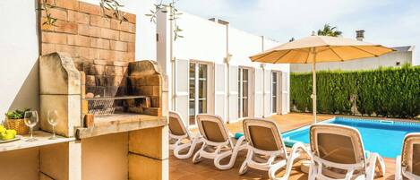 Een terras met een barbecue, lounge stoelen en een zwembad.