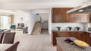A modern kitchen with wooden cabinets and a granite countertop, a dining area with a table and chairs, and a staircase leading to another level.