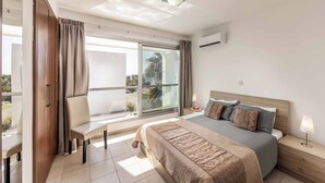 A modern hotel room with a large bed, a desk, and a chair near a sliding glass door.