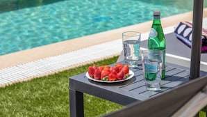 Une table au bord de la piscine, avec une assiette de fraises, deux verres et une bouteille d’eau.